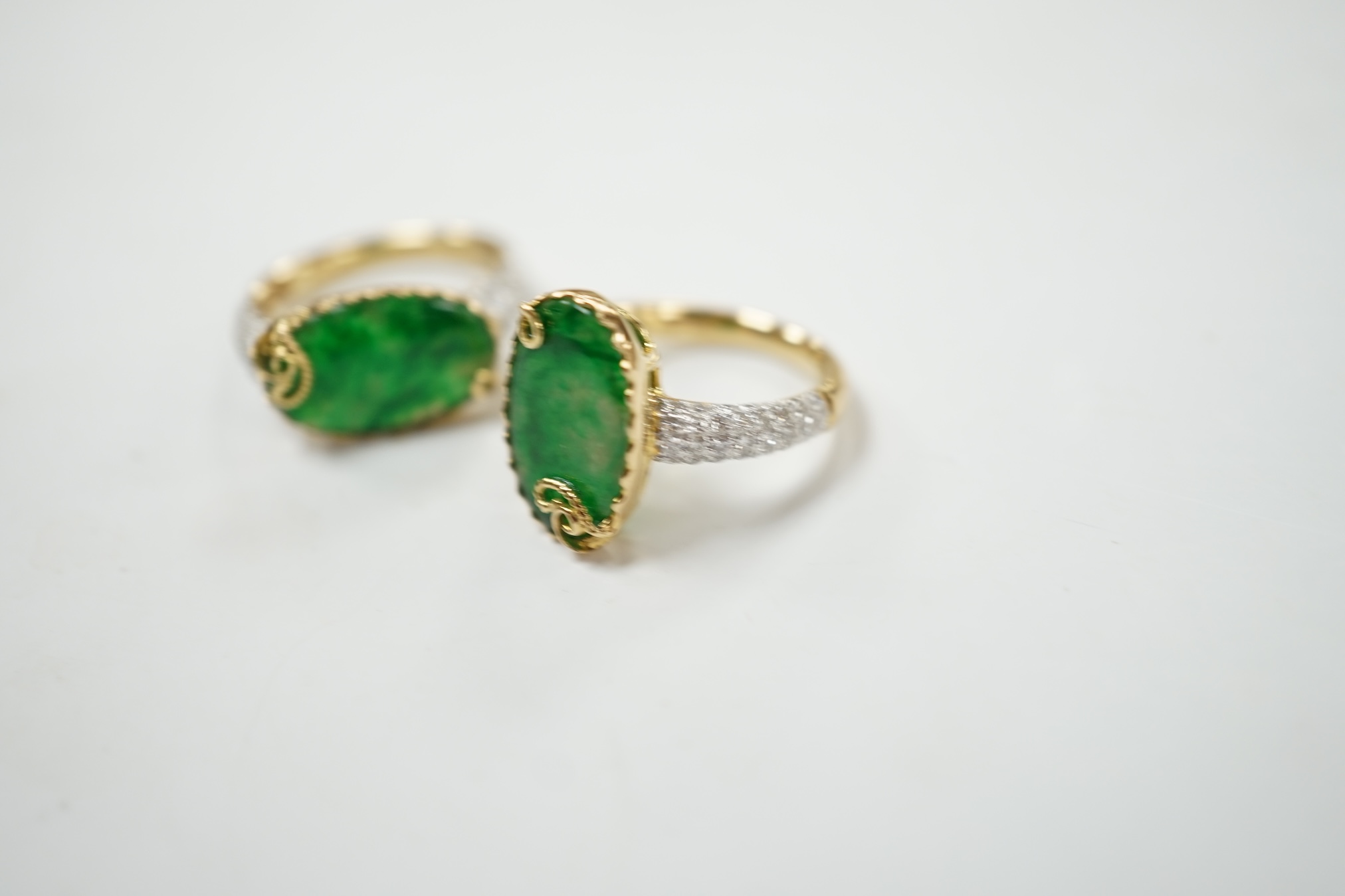 Two similar modern 18k and oval jade set dress rings, with diamond chip set shoulders, sizes K & L, gross weight 9.9 grams. Condition - good